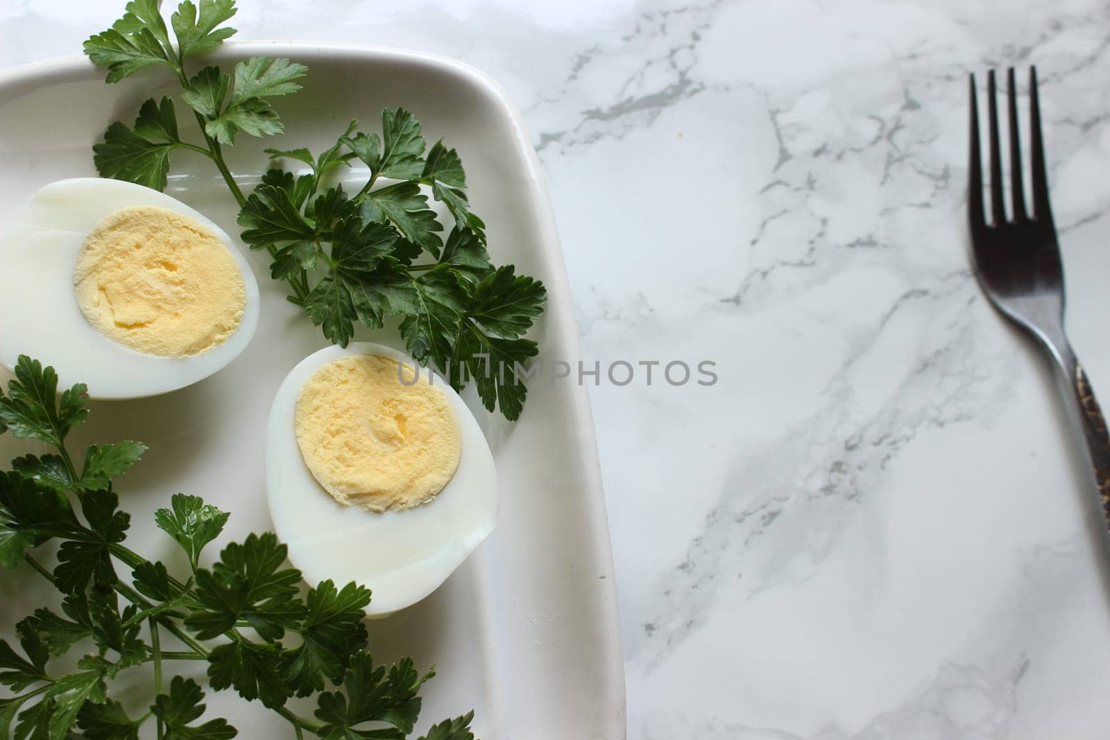 Boiled chicken egg and parsley on a white plate on a marble background.