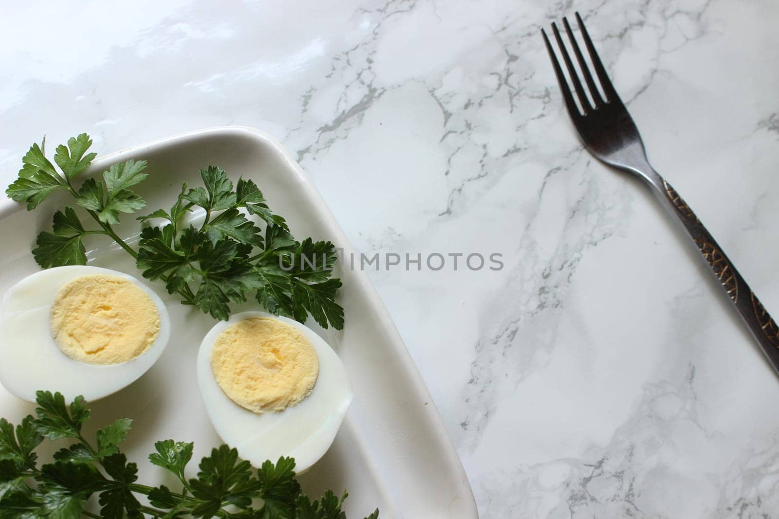 Boiled chicken egg and parsley on a white plate on a marble background.