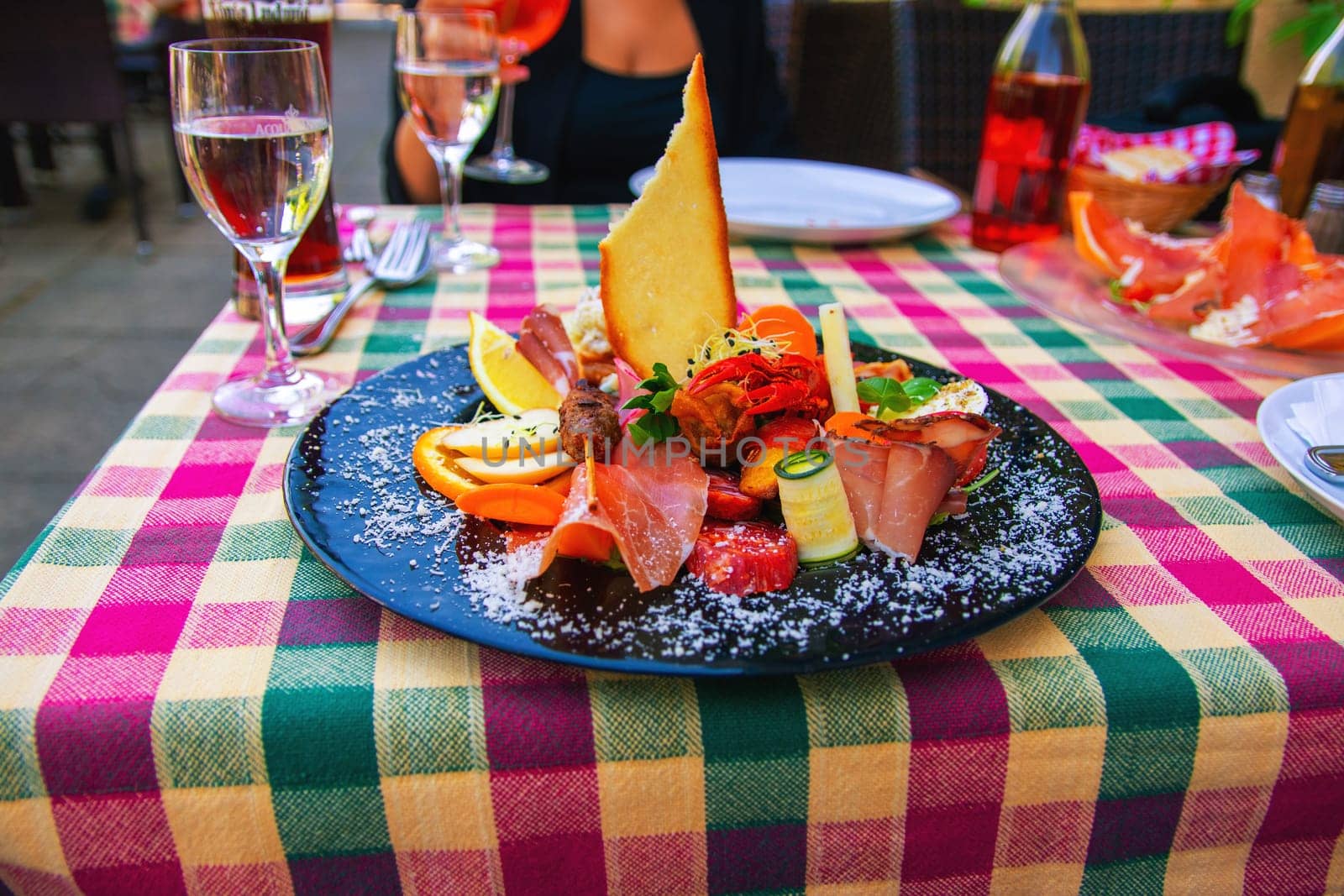 Traditional Italian food. Close-up of mixed Mediterranean appetizers or antipasto and tapas with ham vegetables and crab on black plate on restaurant table.