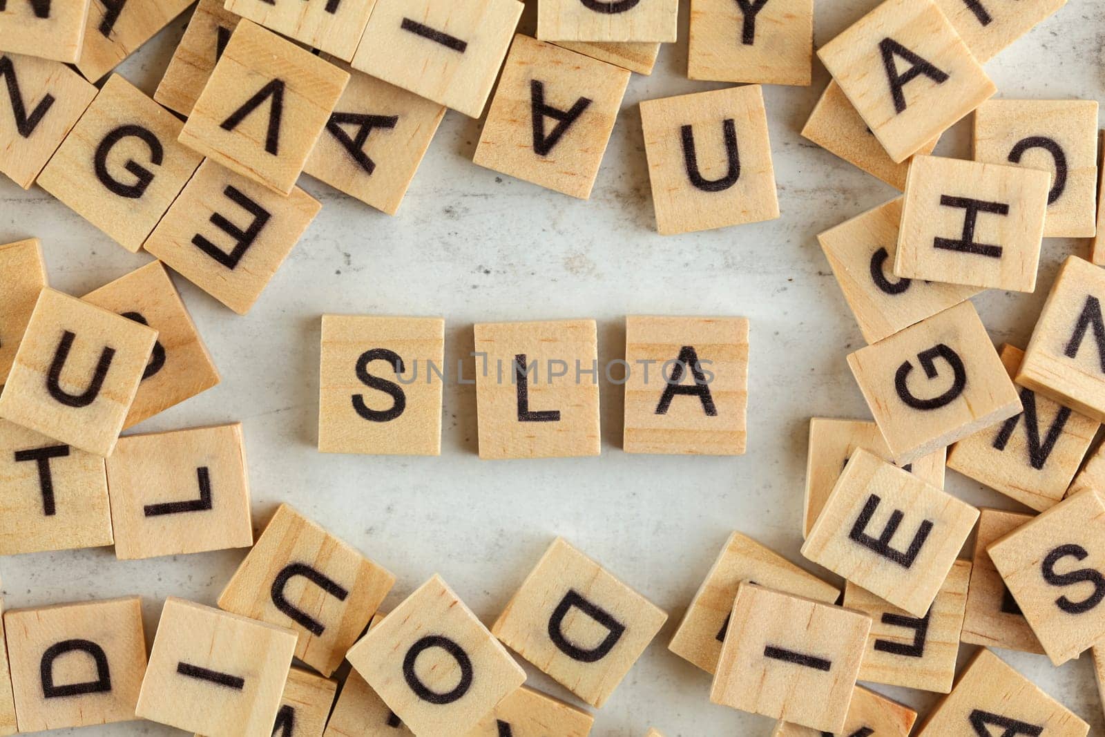 Top down view, pile of square wooden blocks with letters SLA (stands for Service Level Agreement) on white board.