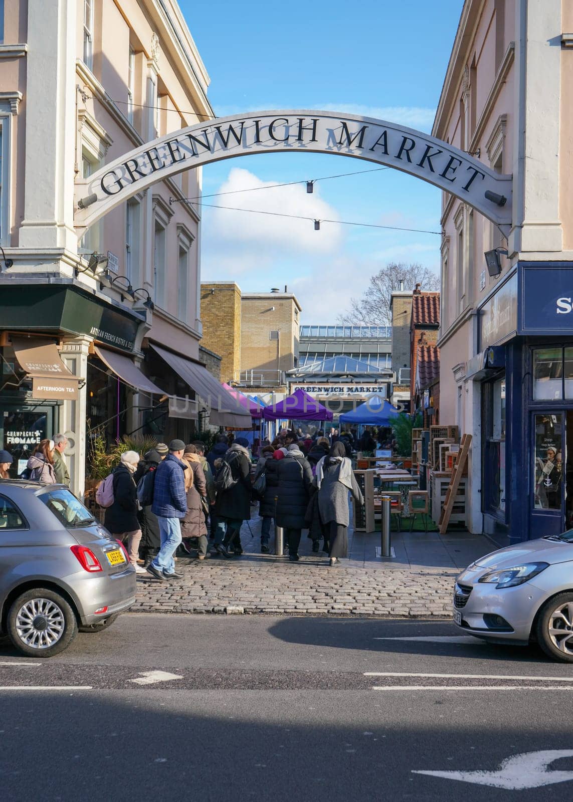 London, United Kingdom - February 02, 2019: People visiting Greenwich Market (World Heritage Site) on sunny Saturday morning, walking to stalls from the street, passing under large sign.