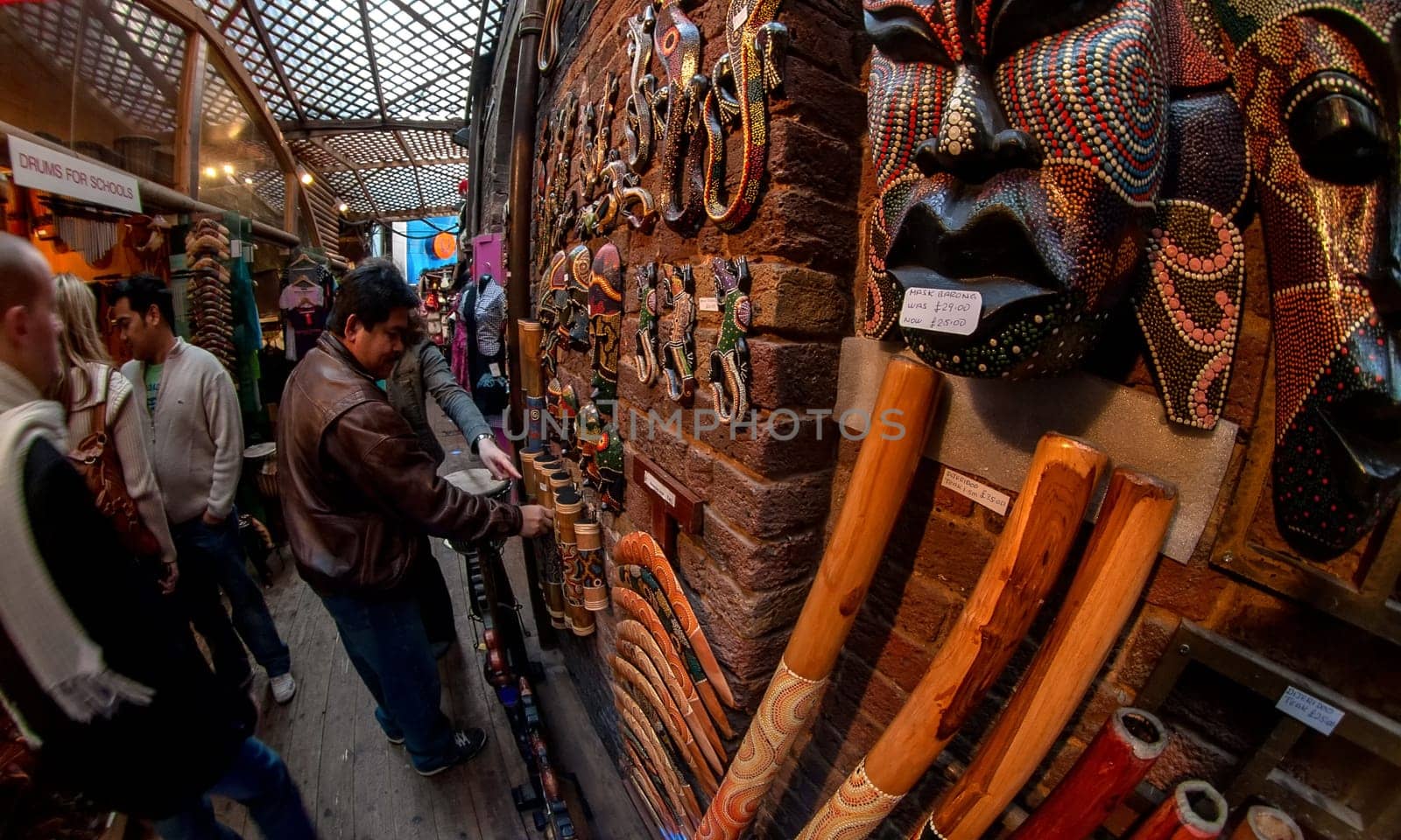 London, United Kingdom - March 31, 2007: Unknown shoppers looking at goods (Aboriginal musical instruments) at Camden Lock, famous market at UK capital. Extreme wide perspective fisheye photo.