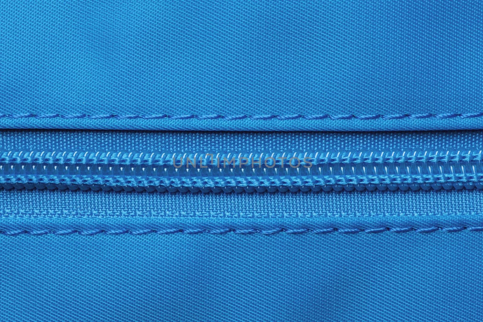 Zip fastener background texture. A high-resolution close-up of a detail from a closed plastic zip fastening on a backpack made of an elastic blue nylon fabric. Macro photo.