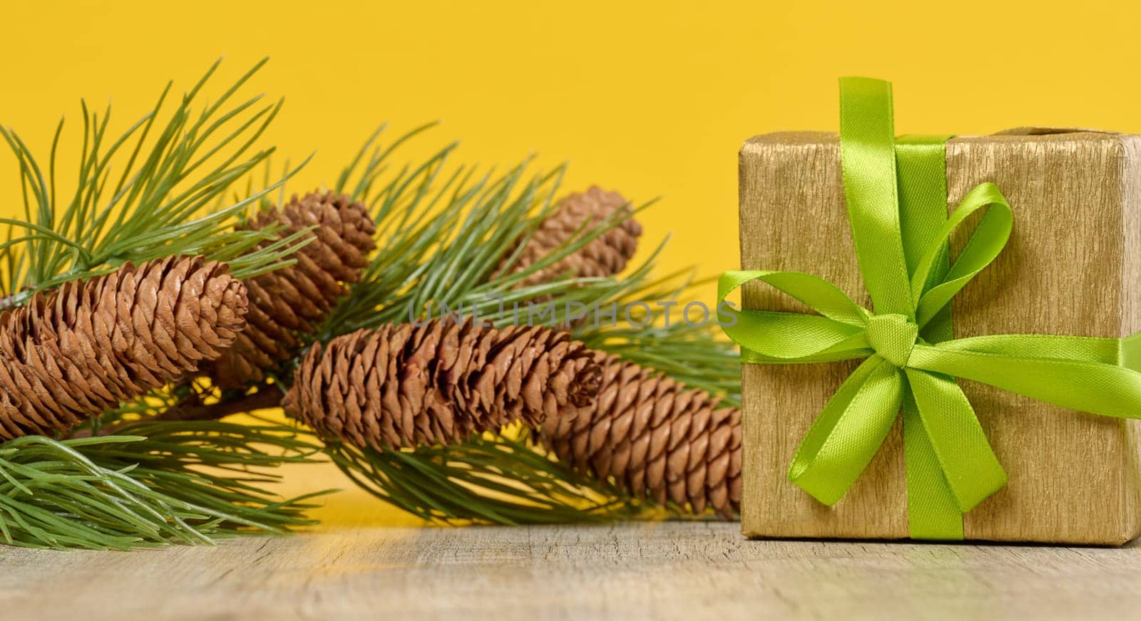 Box with a gift and a spruce branch with cones on a yellow background