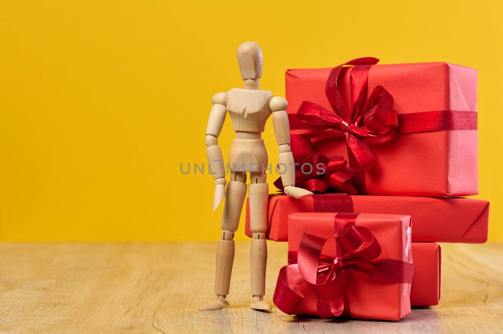 Stack of gifts and wooden mannequin on yellow background, holiday