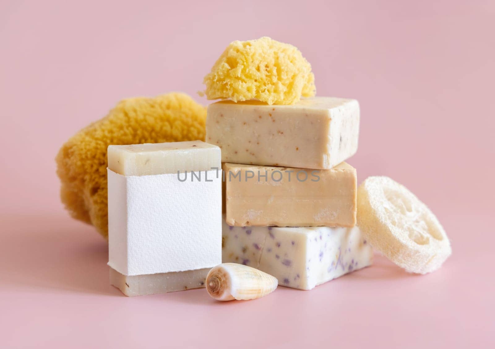 Beige handmade soap bars with blank label, natural sponge and seashell on light pink close up, packaging mockup, copy space. Herbal products for face and body care
