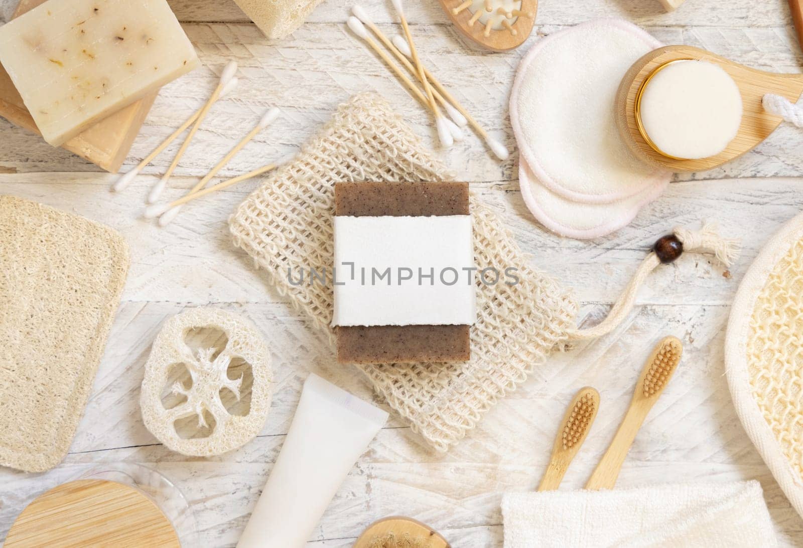 Organic handmade beige soap bar with blank label on soap saver bag near hygiene Items - natural sponges and brush, bamboo toothbrushes and cotton swabs, top view, mockup