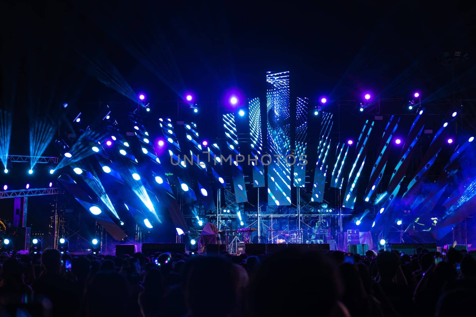 The night comes alive at a concert festival with a jubilant crowd in front of the brilliantly lit stage. The lens flare captures the excitement as unrecognizable people revel in joy of music event.