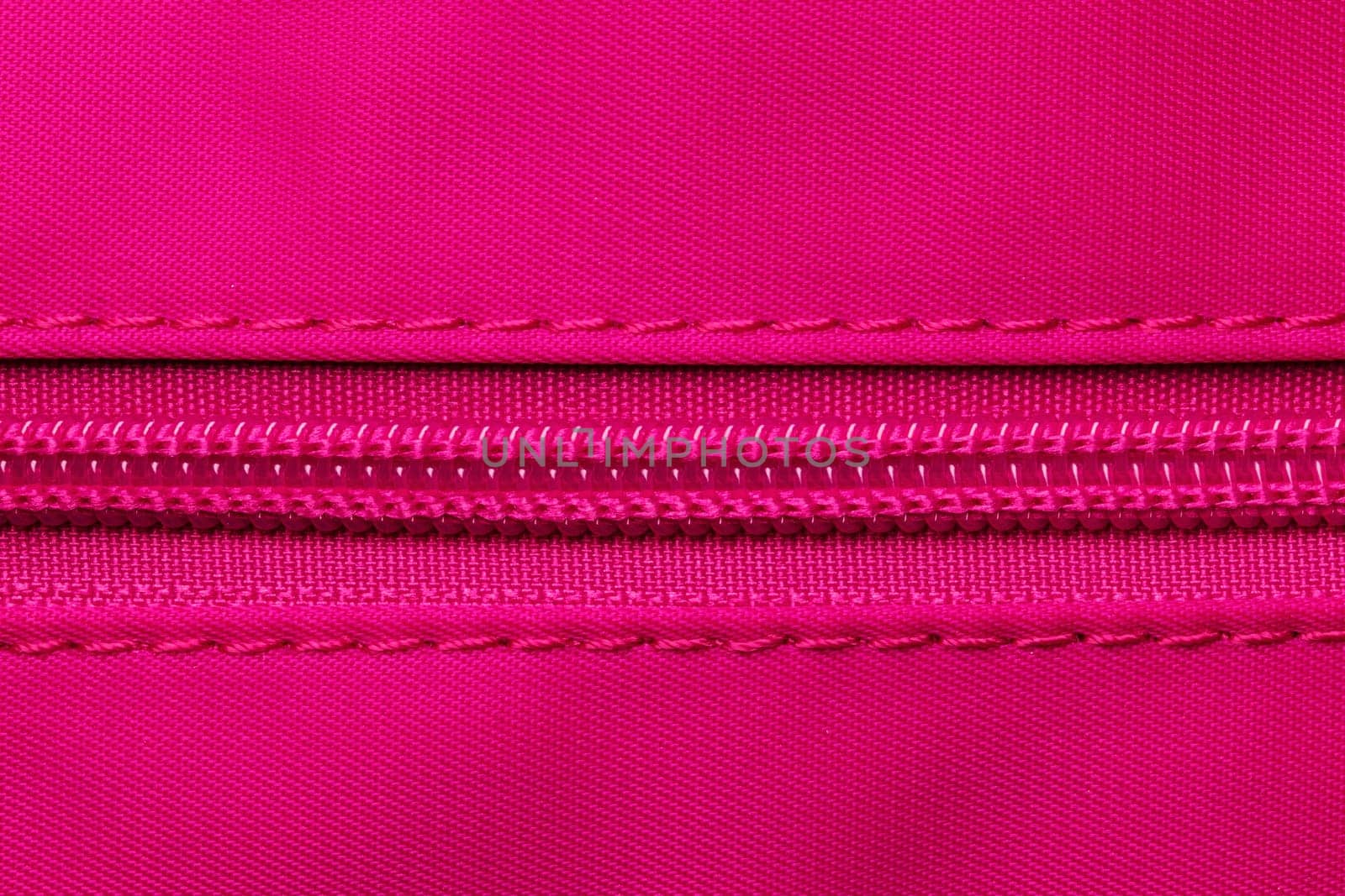 Zip fastener background texture. A high-resolution close-up of a detail from a closed plastic zip fastening on a backpack made of an elastic pink nylon fabric. Macro photo.