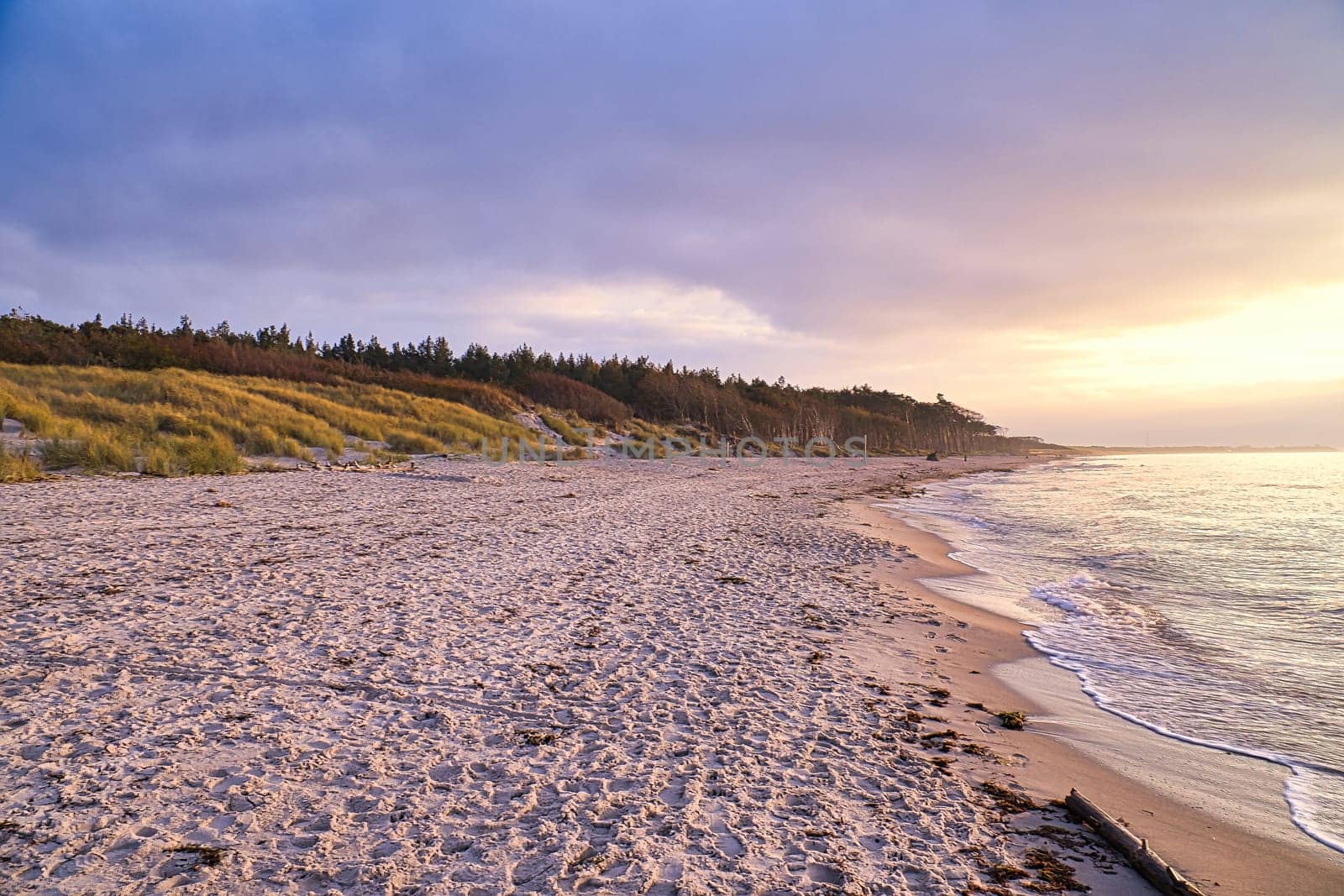 Sunset on the west beach on the Baltic Sea. Waves, beach, cloudy sky and the last rays of sunshine on the coast. Landscape photo