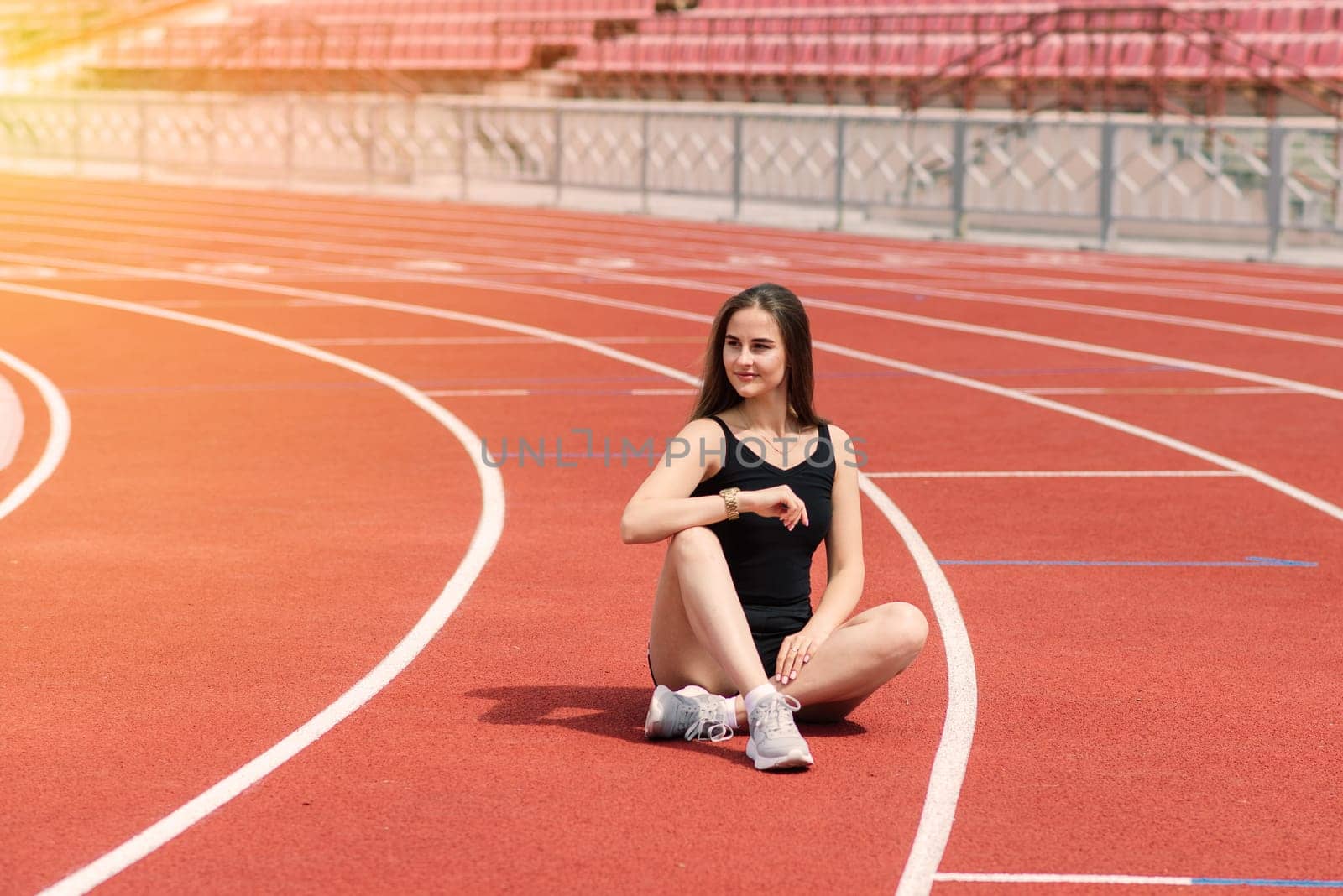 A female coach with dark hair stands on the red running track of the stadium, dressed in sports uniform.