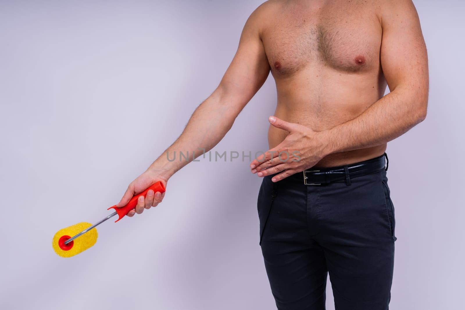 Cheerful young topless man hold paint roller isolated on a grey background studio.