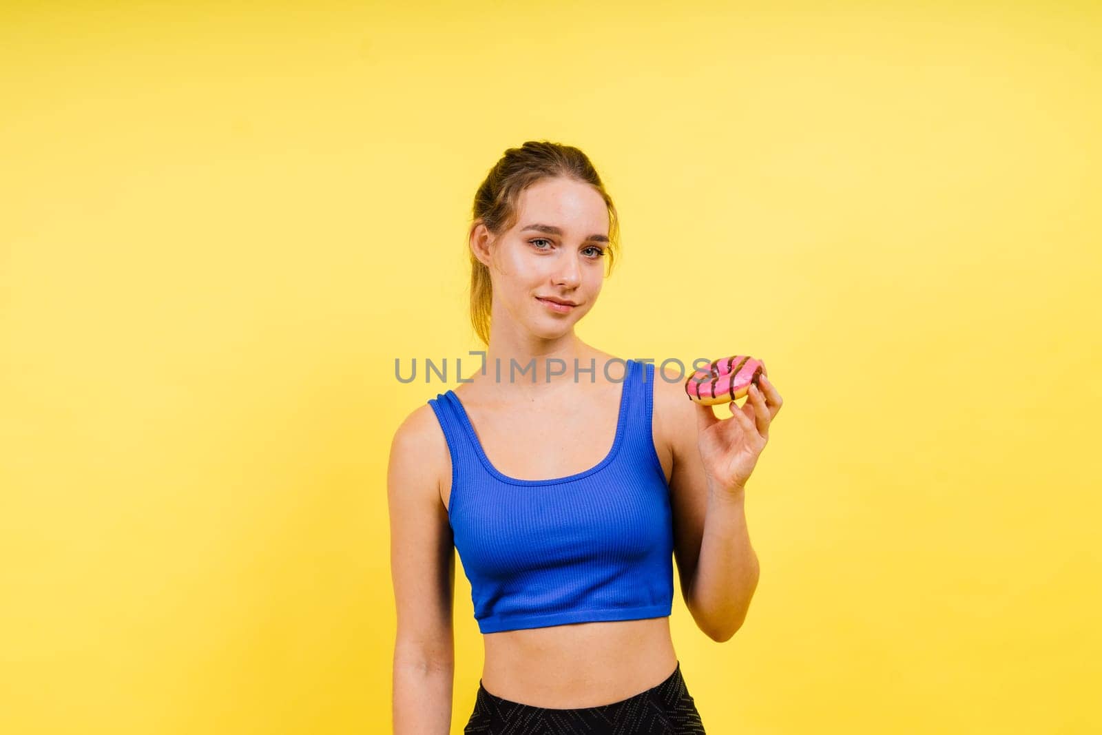 Lovely young caucasian woman in a sports wear with donuts on grey and yellow studio background.