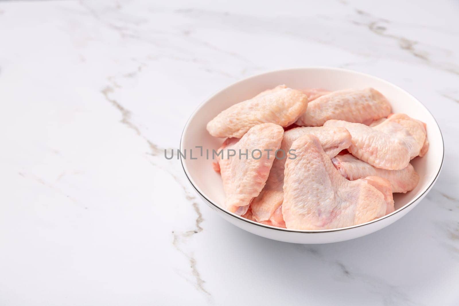 Raw chicken wings in white bowl, prepared for cooking on marble background