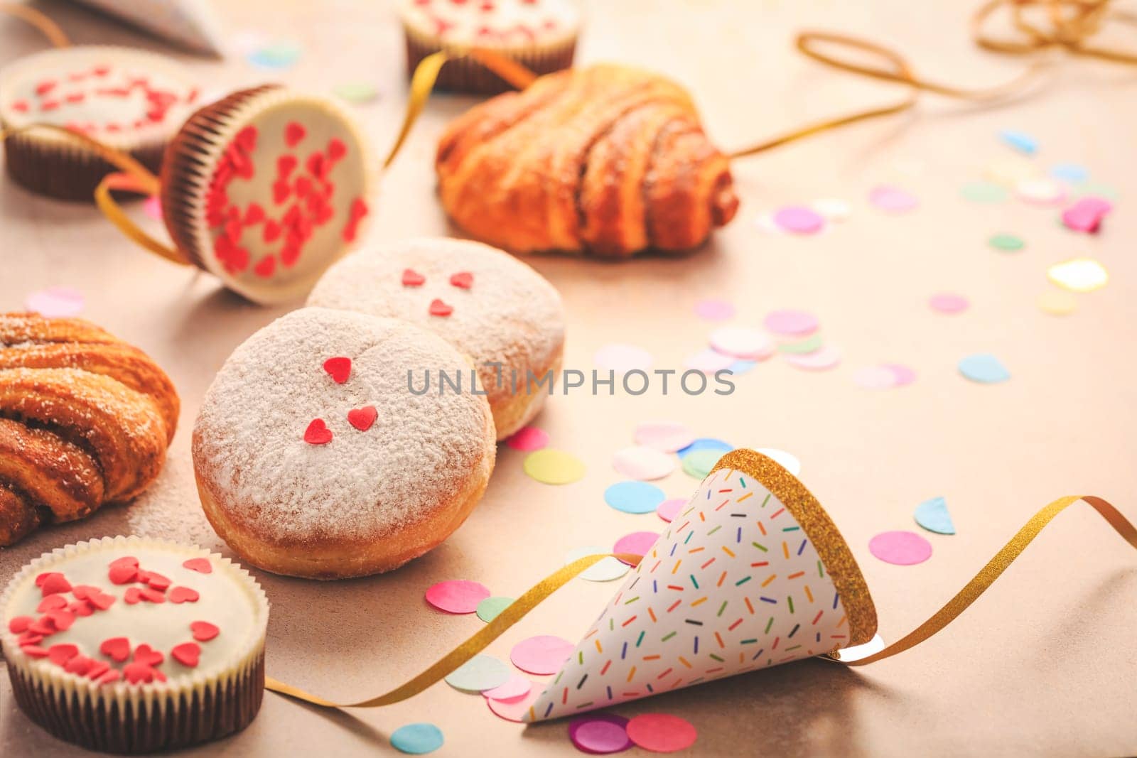 Berliner, cinnamon rolls and cupcakes for carnival and party. German Krapfen or donuts with streamers and confetti. Colorful carnival or birthday image