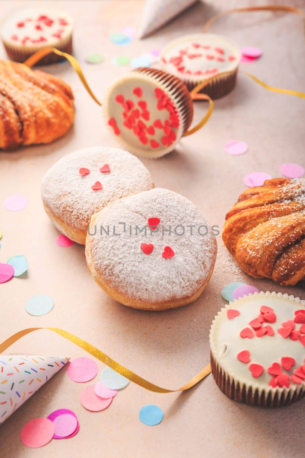 Berliner, cinnamon rolls and cupcakes for carnival and party. German Krapfen or donuts with streamers and confetti. Colorful carnival or birthday image
