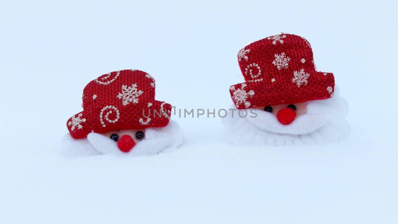 Two Christmas decorations of the head of Santa Claus on white snow