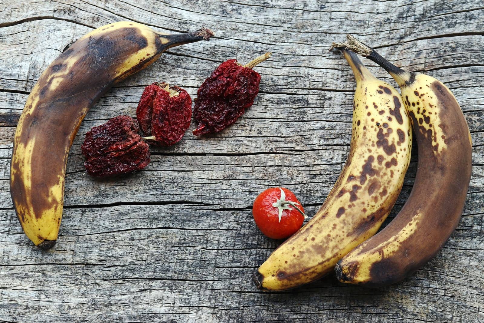 Old brown dried bananas, peppers and tomatoes on a wooden base