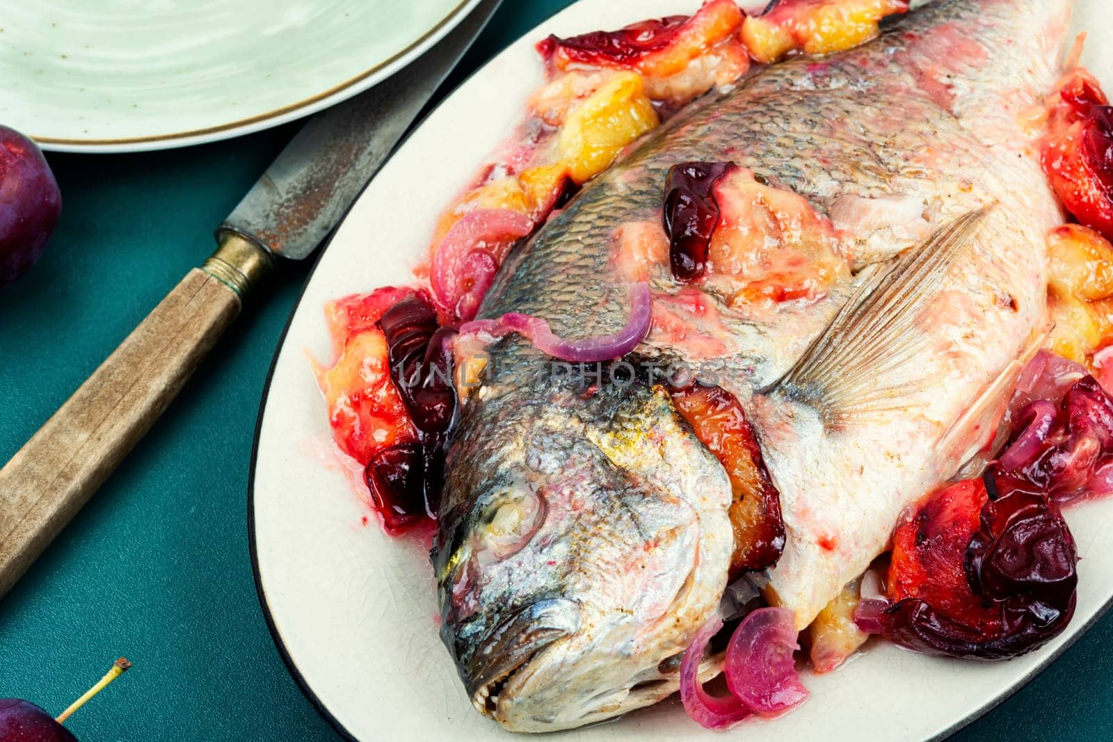 Dorado or sea bream fish baked with plums. Gilthead fishes
