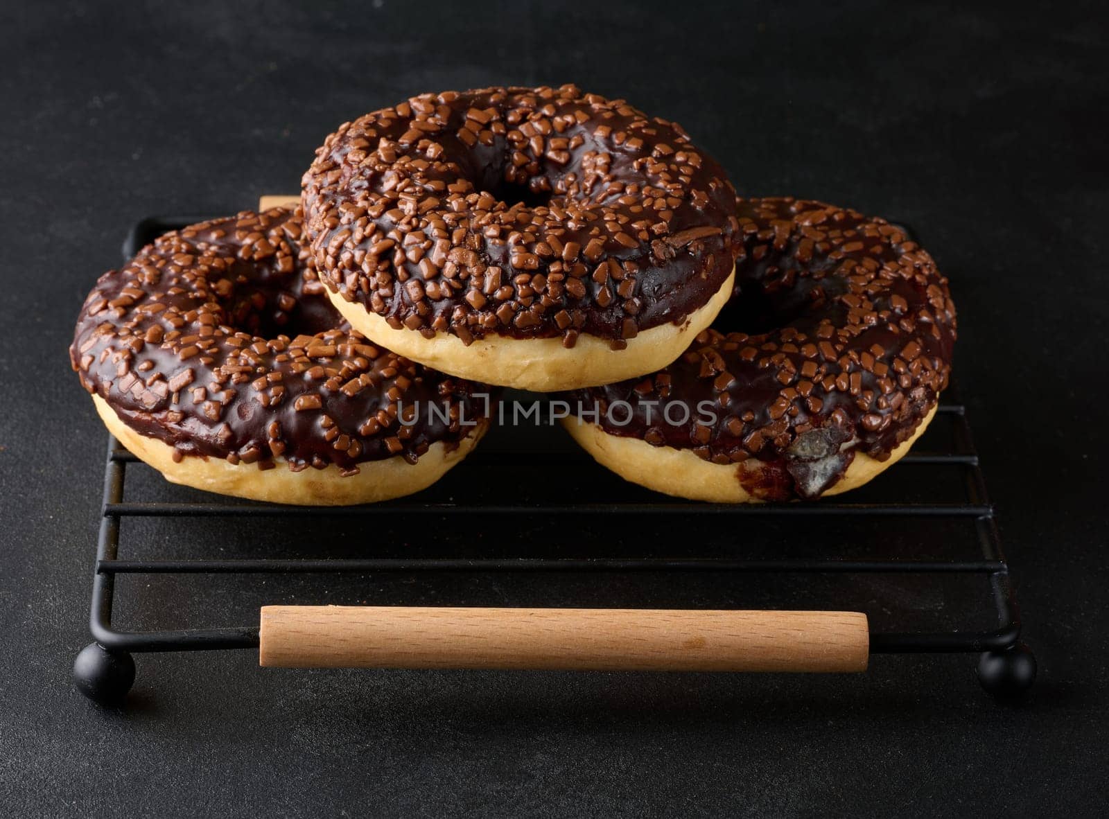 Chocolate donuts sprinkled with crushed nuts on a black table