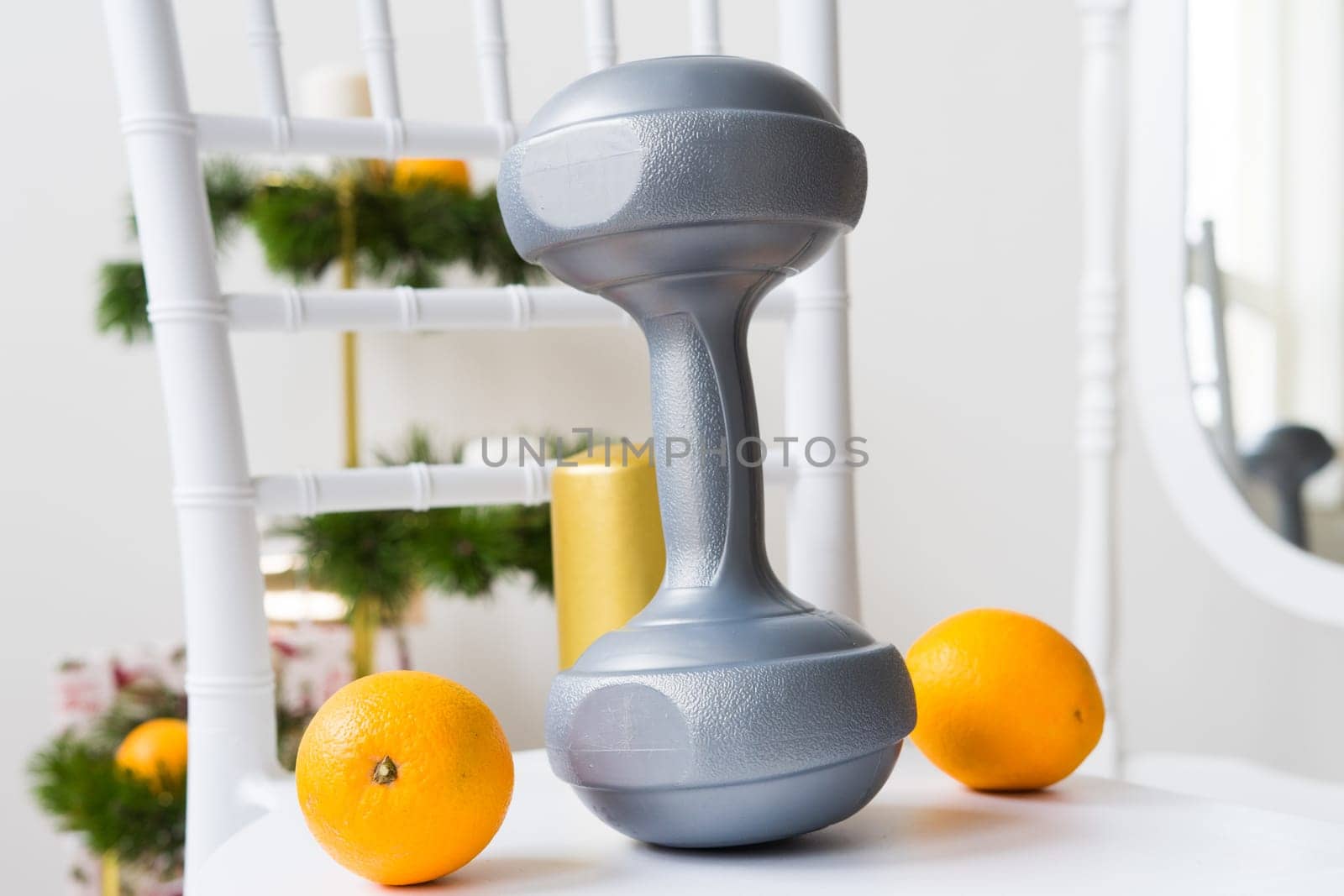 Sports equipment: dumbbell, boxing gloves, fir branch, Christmas ornament, gifts on a chair.