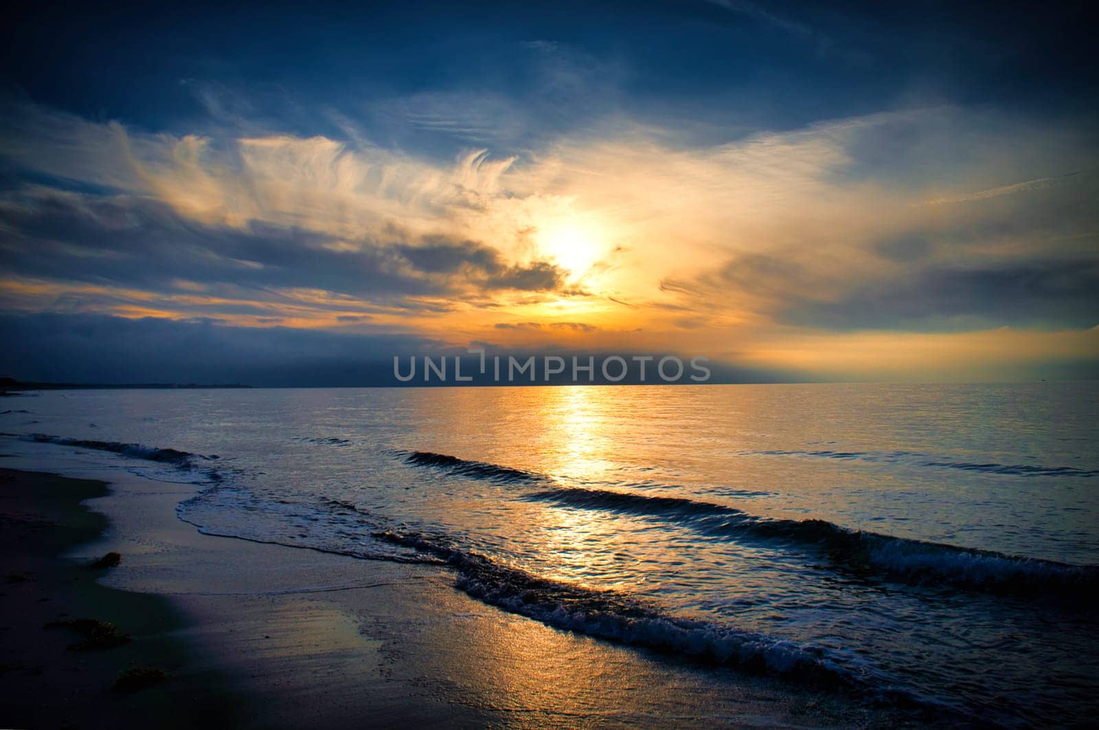 Sunset on the west beach on the Baltic Sea. Waves, beach, cloudy sky and the last rays of sunshine on the coast. Landscape photo