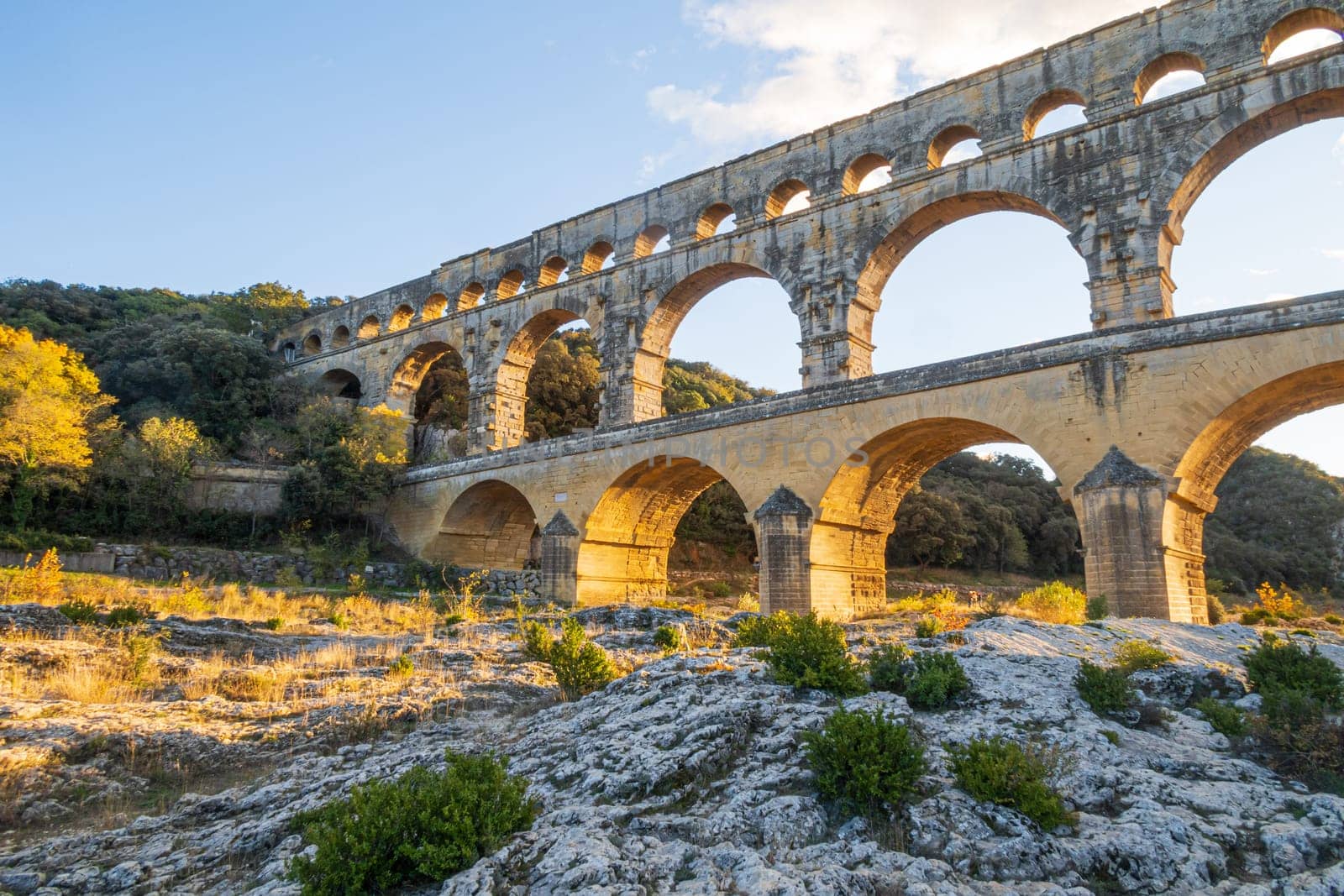 The magnificent Pont du Gard at setting sun. Ancient Roman three-tiered aqueduct bridge. Built in the 1st century AD to carry water to the Roman colony of Nemausus (Nîmes).  Photography taken in Vers-Pont-du-Gard, Provence, southern France.