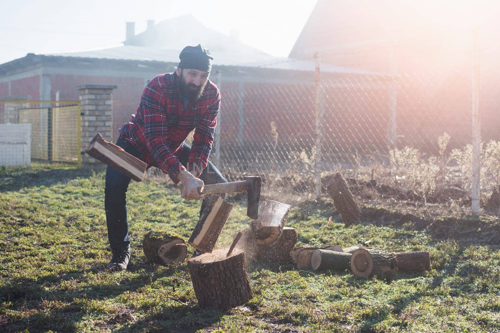 The bearded lumberjack worker or woodcutter is cutting wood or firewood with axe outdoors.
