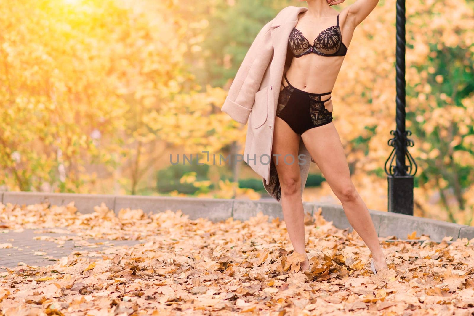 Young beautiful dark-haired woman with a slender figure posing in lingerie and a classic coat in an autumn park