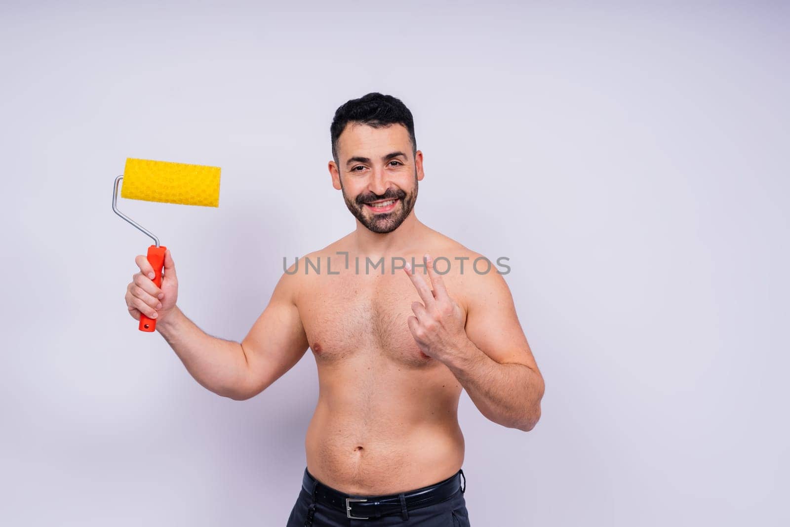 Cheerful young topless man hold paint roller isolated on a grey background studio.