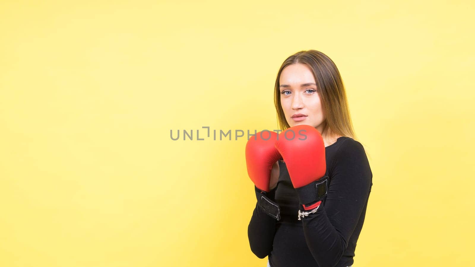 Portrait of young woman in a casual clothes and hands in boxing gloves against yellow background