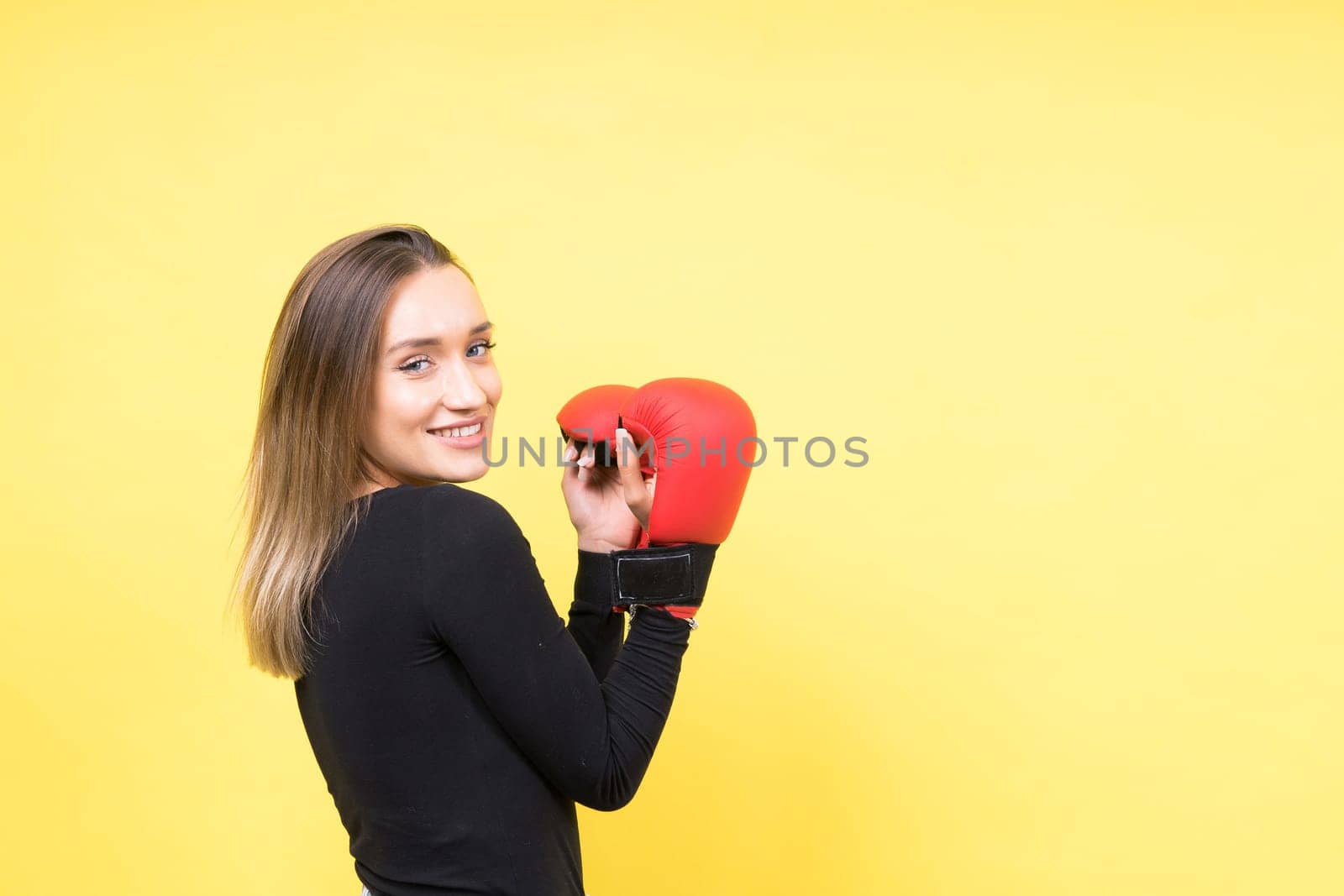 Portrait of young woman in a casual clothes and hands in boxing gloves against yellow background