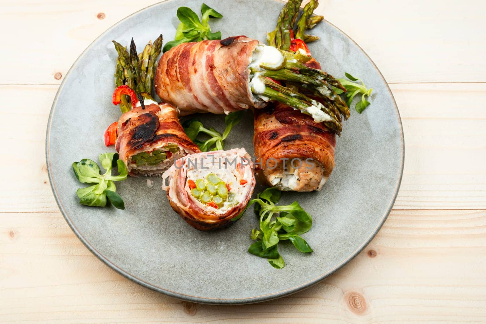 Roast meat rolls stuffed with green young asparagus on wooden table.