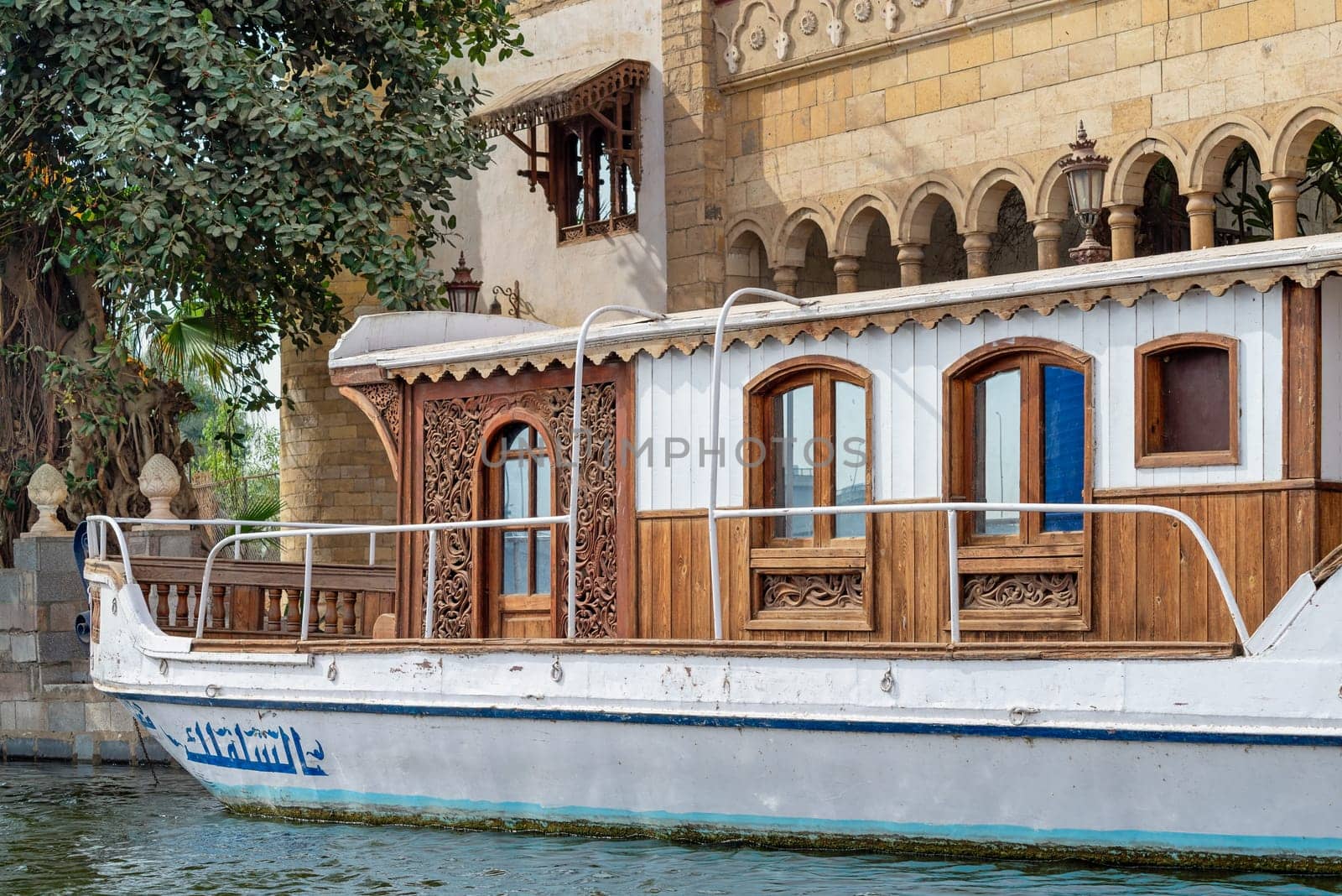 Vibrant weathered wooden antique boat, rests peacefully on River Nile infront of a Mamluk style Palace of Prince Naguib Hassan Abdallah, Dahab Island, Cairo, Egypt