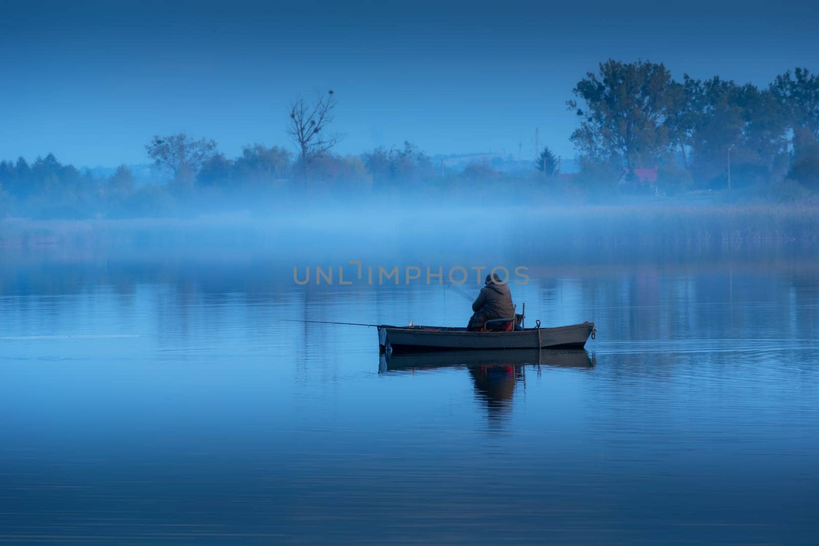 Angler in a boat and fog on a calm blue lake