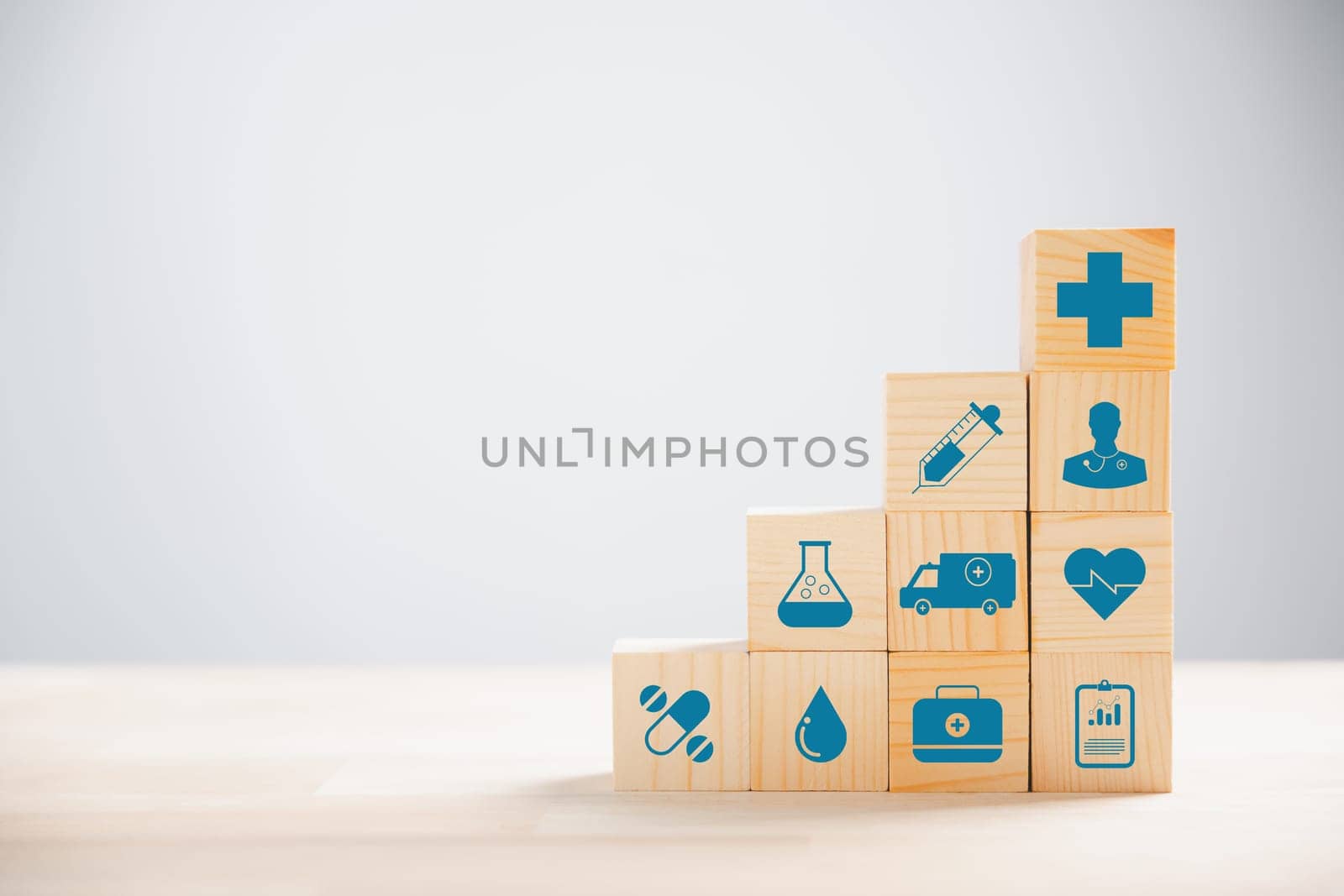 Representation of healthcare and insurance via pyramid-stacked wooden cubes. Crowning medical insurance icon suggests safety. Blue background presents copyspace for Health Insurance communication.