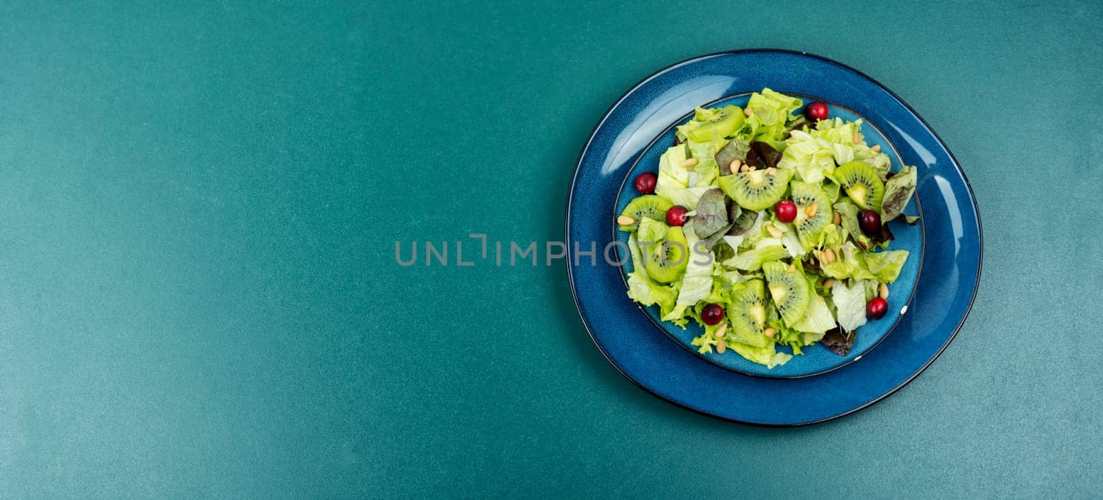 Fresh salad of kiwi, leafy greens, berries and pine nuts on the table. Clean eating.
