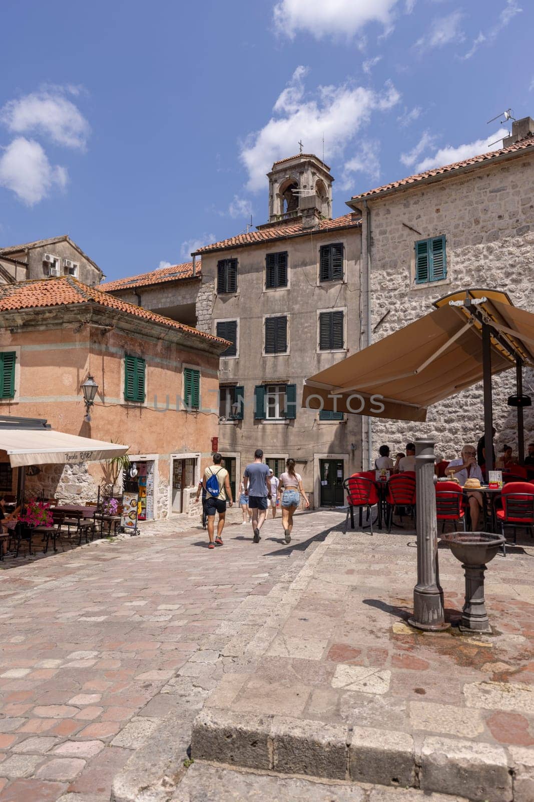 Kotor, Montenegro - June 26, 2023:  Picturesque small square in the Old Town, surrounded by stone tenement houses, with outside restaurants and old metal well, Kotor, Montenegro