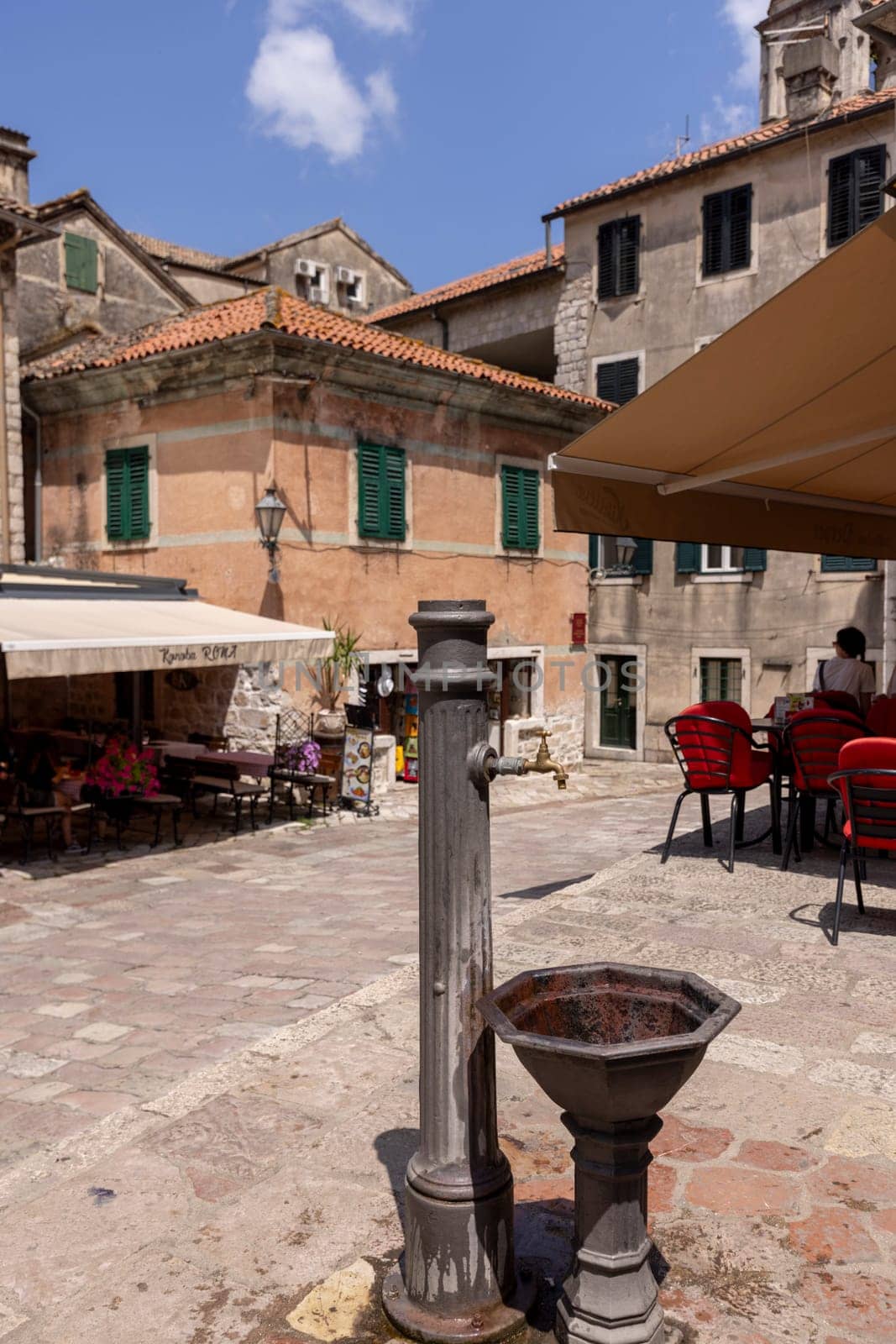 Kotor, Montenegro - June 26, 2023:  Picturesque small square in the Old Town, surrounded by stone tenement houses, with outside restaurants and metal well, Kotor, Montenegro