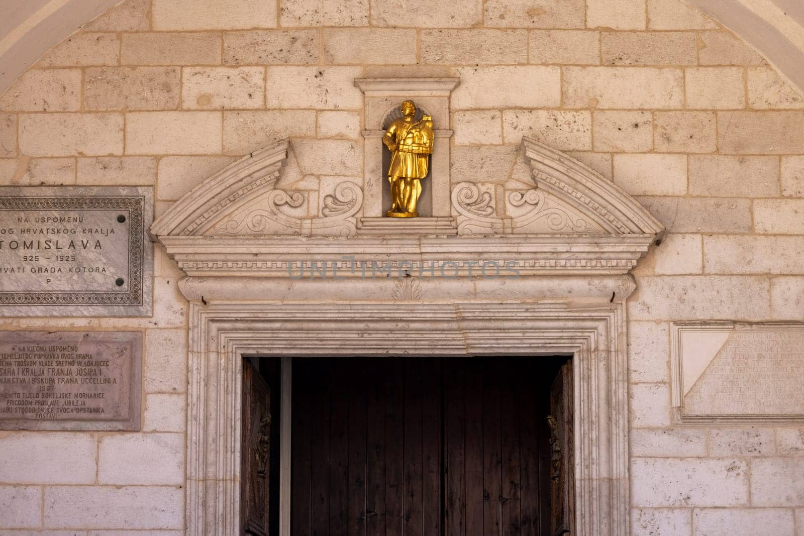 Kotor, Montenegro - June 26, 2023: Facade of Cathedral of Saint Tryphon (Kotor Cathedral), roman catholic medieval church. Entrance door is decorated with a portal with  golden figurine