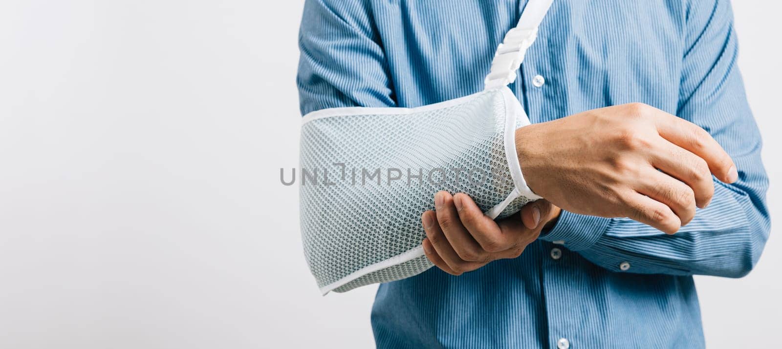 A resilient male with broken arm maintains smile while wearing splint for treatment, coping with discomfort. An upbeat Asian man in an arm sling on white background, symbolizing injury recovery.