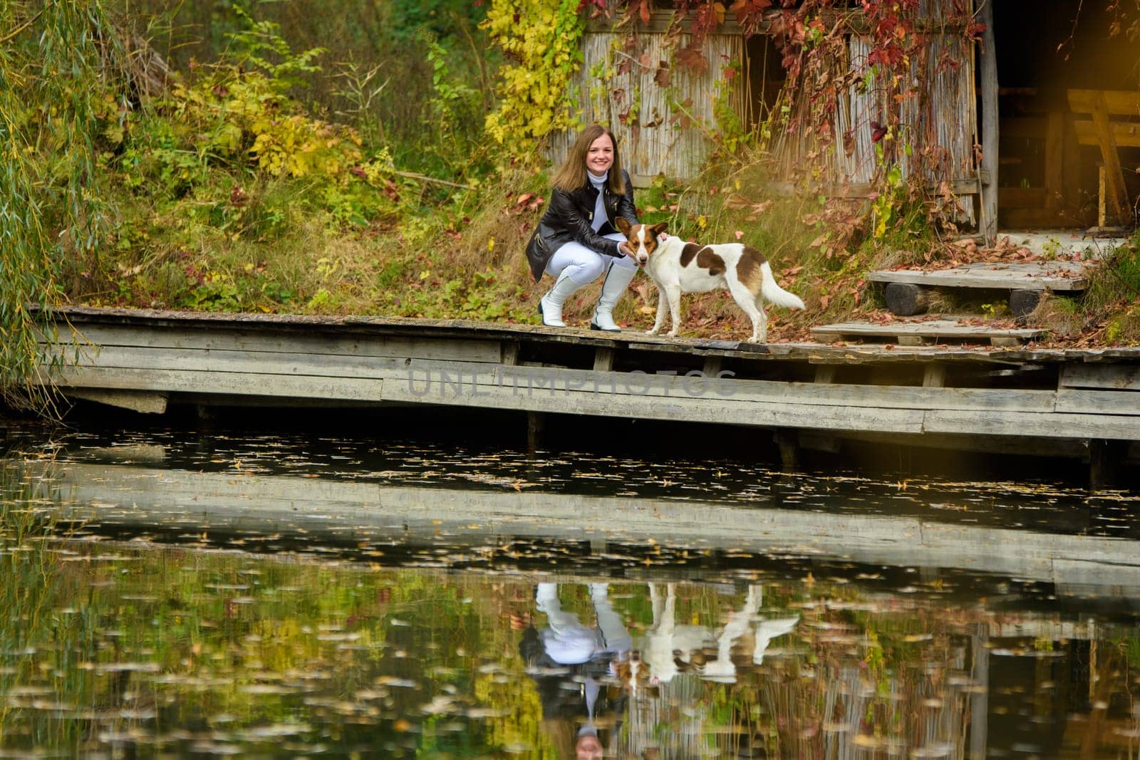 A young beautiful girl walks with a dog near a lake in an autumn park