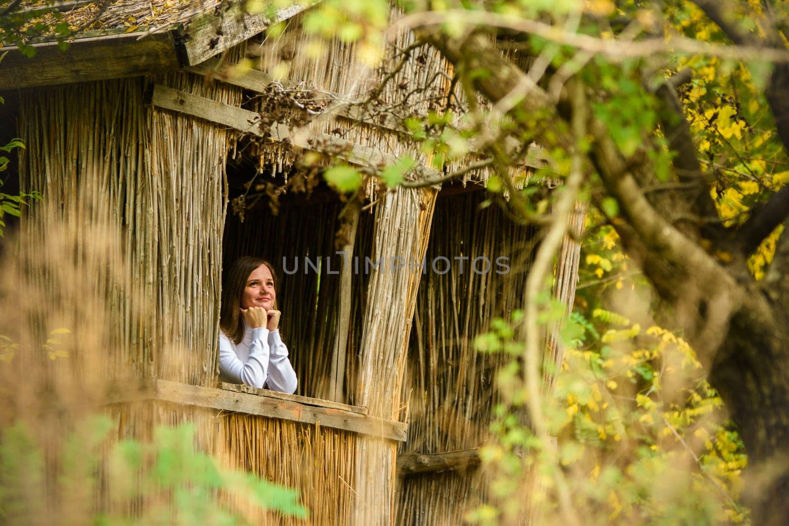 A young beautiful girl looks out of the window of an old house in the forest