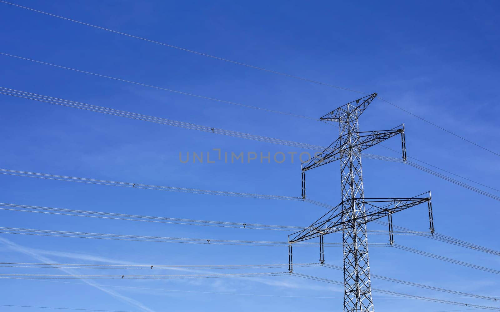 Looking up to steel electricity pylon against blue sky with only few clouds streaks
