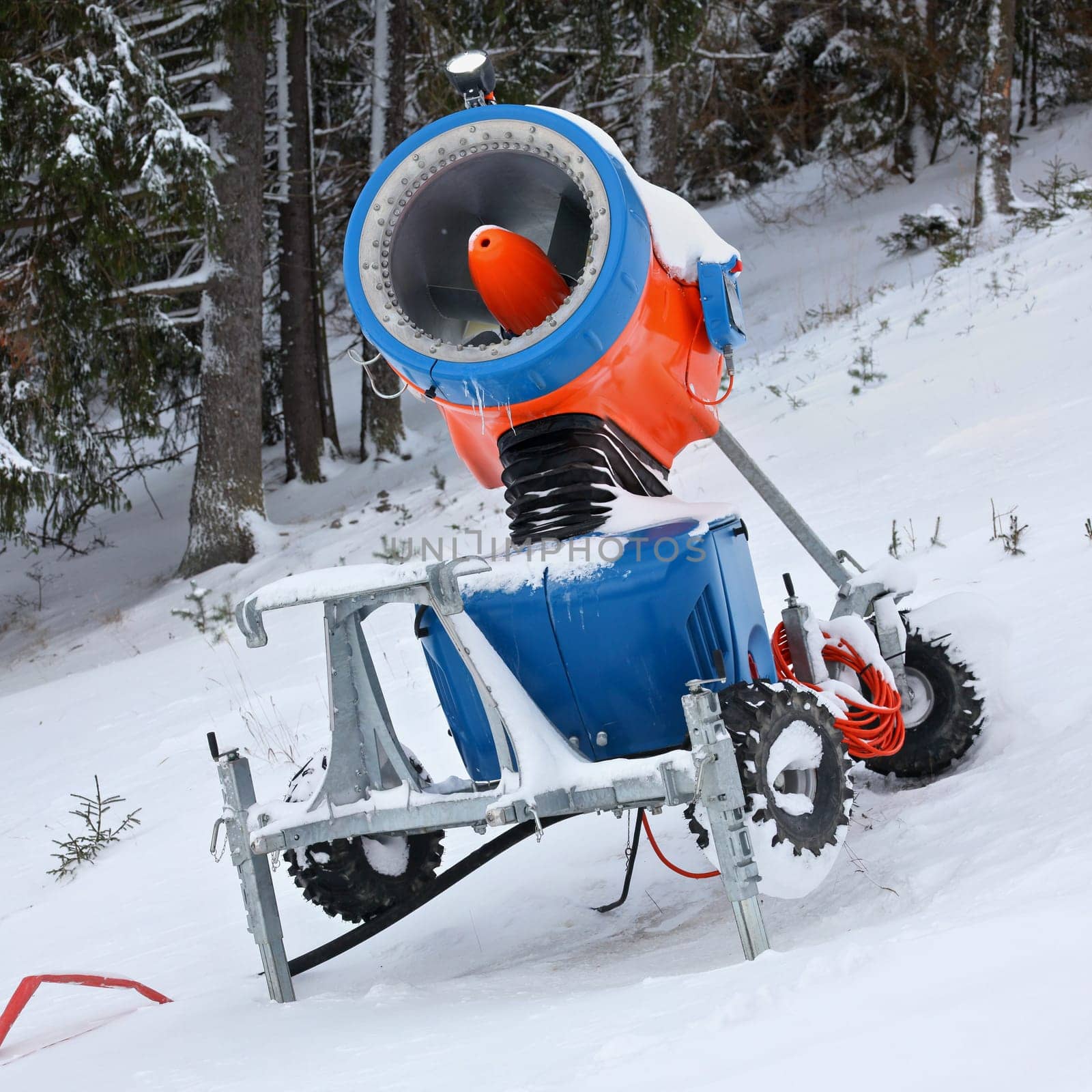 Bright orange and blue snow making cannon, trees in background