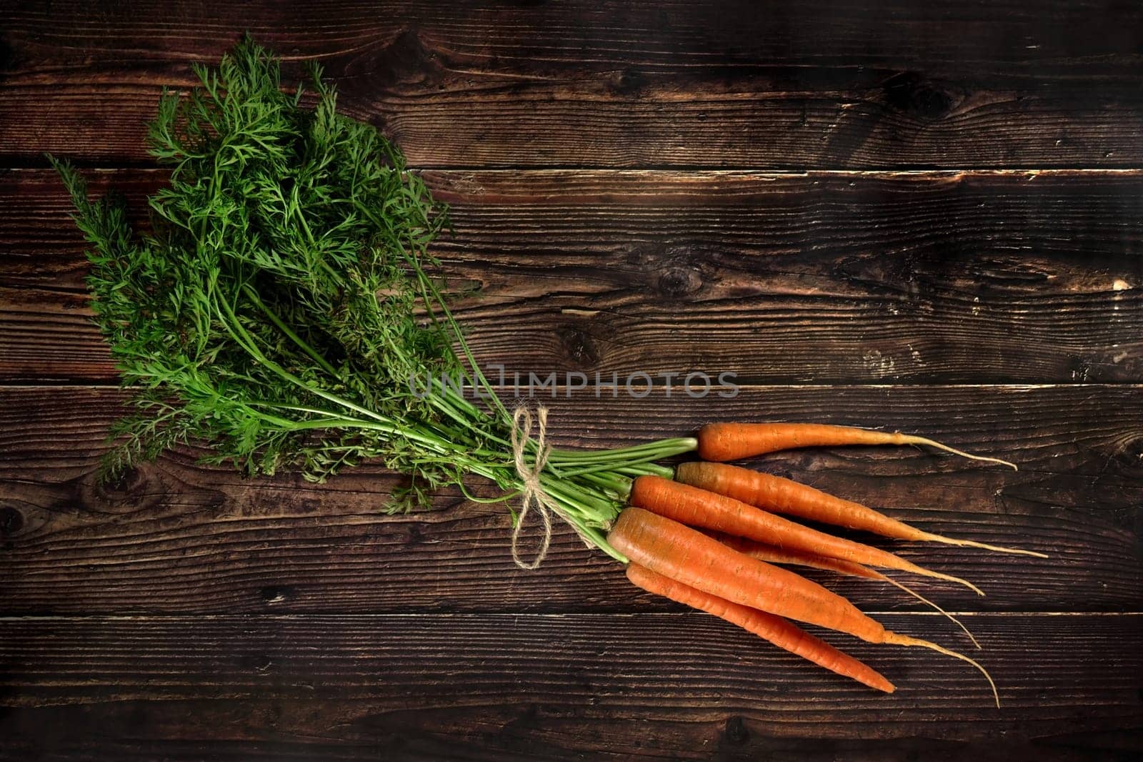 Bunch of carrots with leaves on dark wooden board, view from above