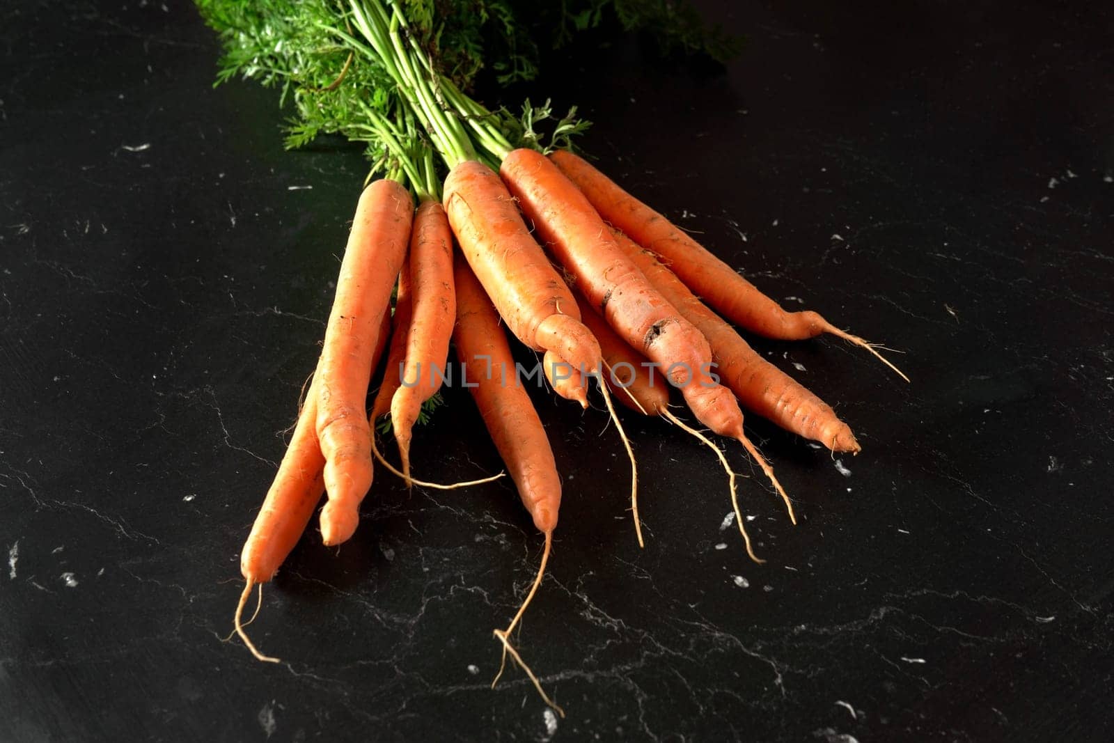 Bunch of organic raw carrot with green leaves on black marble like board, view from above