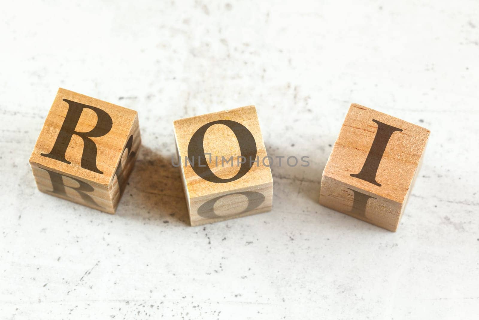 Three wooden cubes with letters ROI (stands for Return on Investment) on white board.