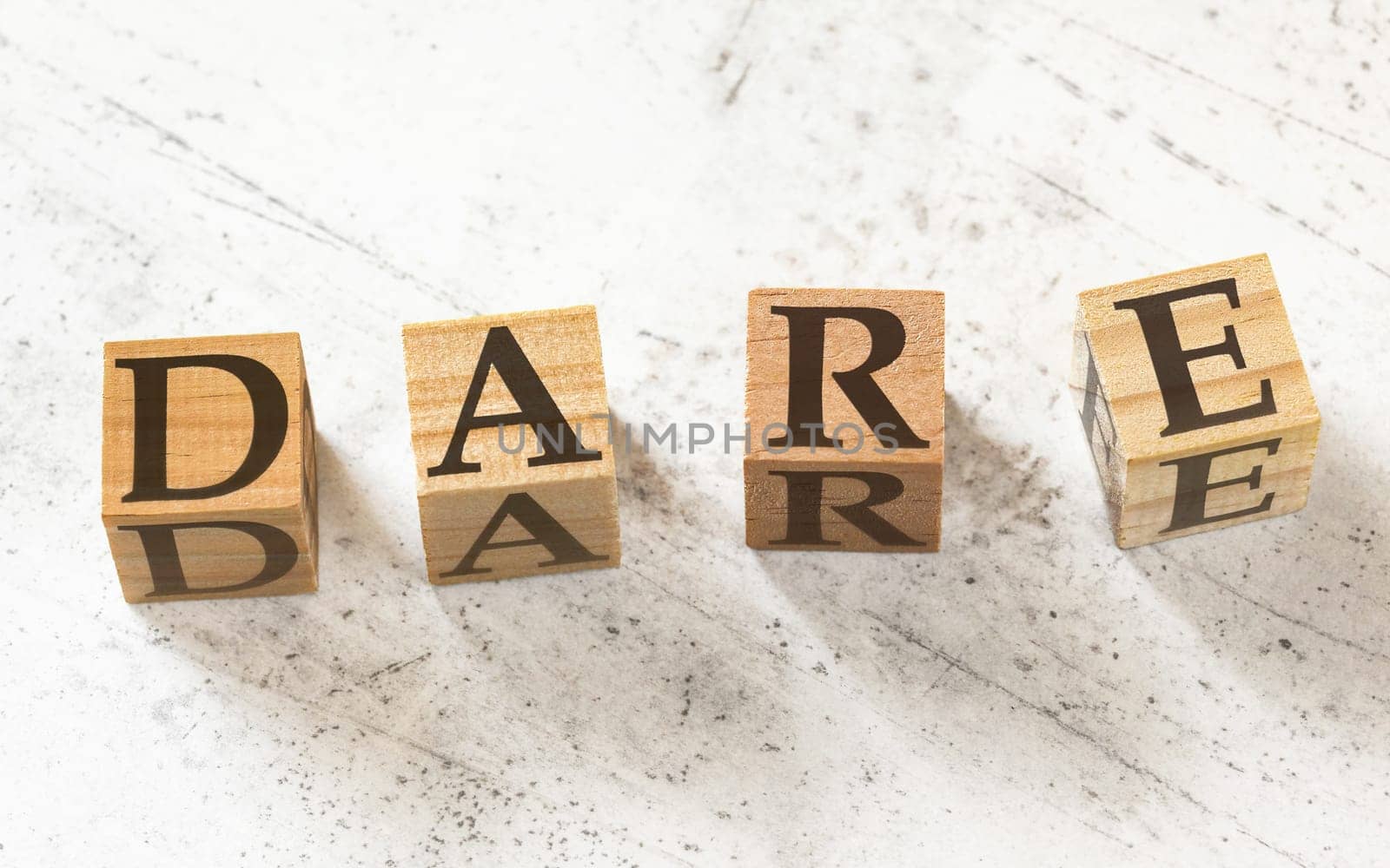 Four wooden cubes with letters DARE (stands for decision-making model -Define, Assess, Respond, Evaluate) on white working board.