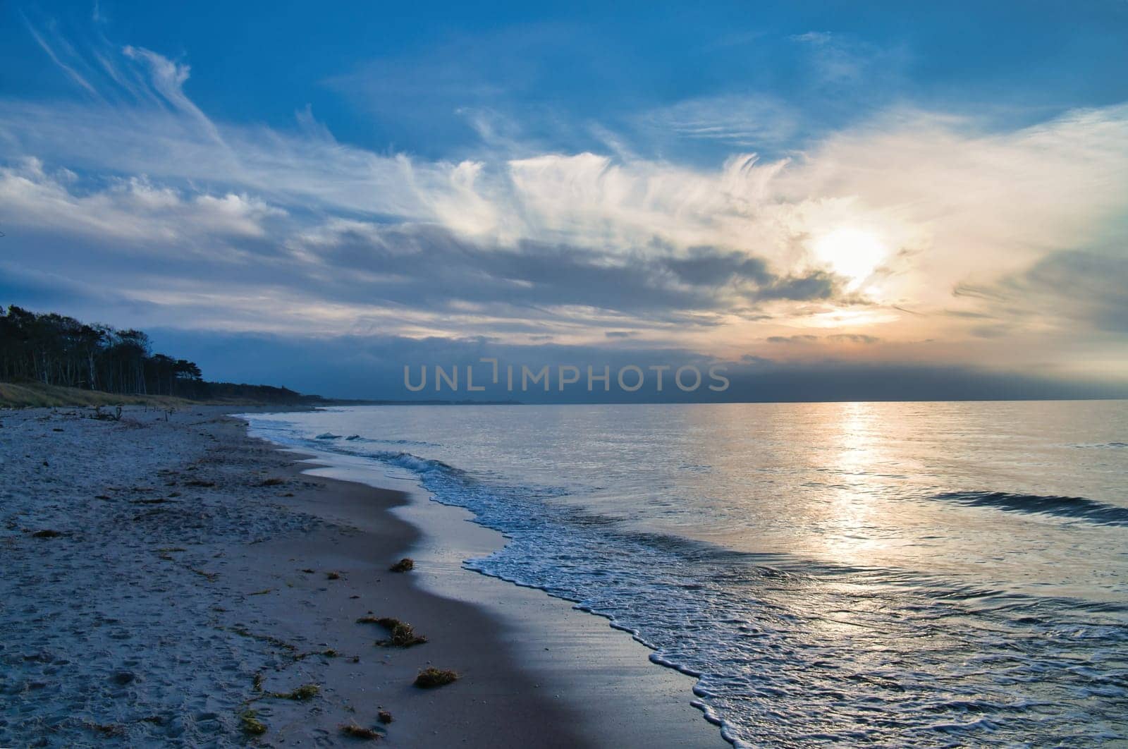 Sunset on the west beach on the Baltic Sea. Waves, beach, cloudy sky and the last rays of sunshine on the coast. Landscape photo